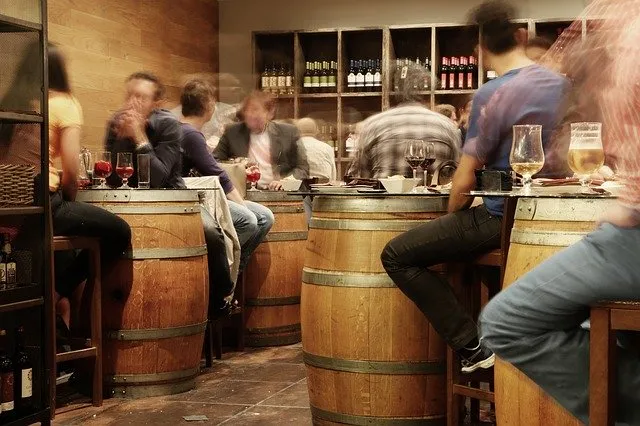 Gente tomando vino alrededor de barricas en un bar